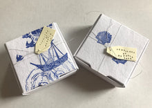 Load image into Gallery viewer, Beautiful handmade sea themed recyclable packaging/jewellery box. Features sea shells, boat, birds, waves. Blue and white colours. Hand stamped labels all tied together with silver thread.